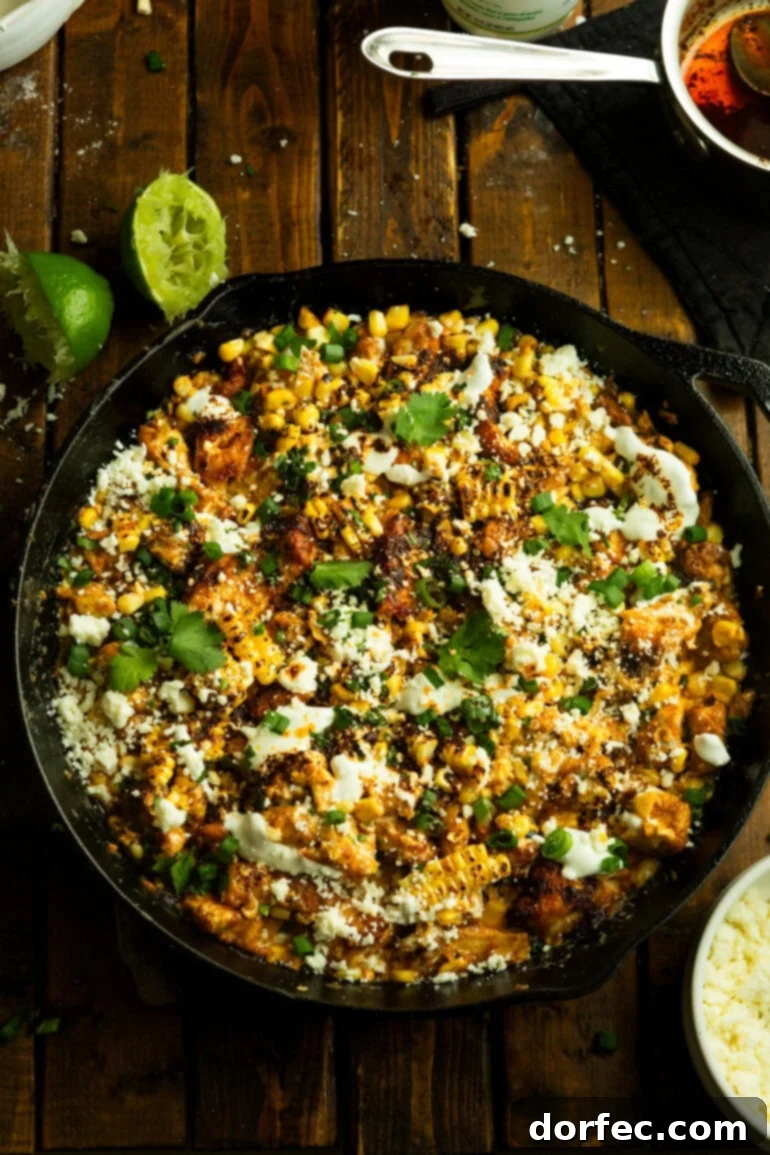 Creamy Mexican Street Corn Chicken Skillet 11 An overhead view of a cast iron skillet filled with chunks of tender cooked chicken mixed with charred Mexican street corn, garnished with fresh cilantro.