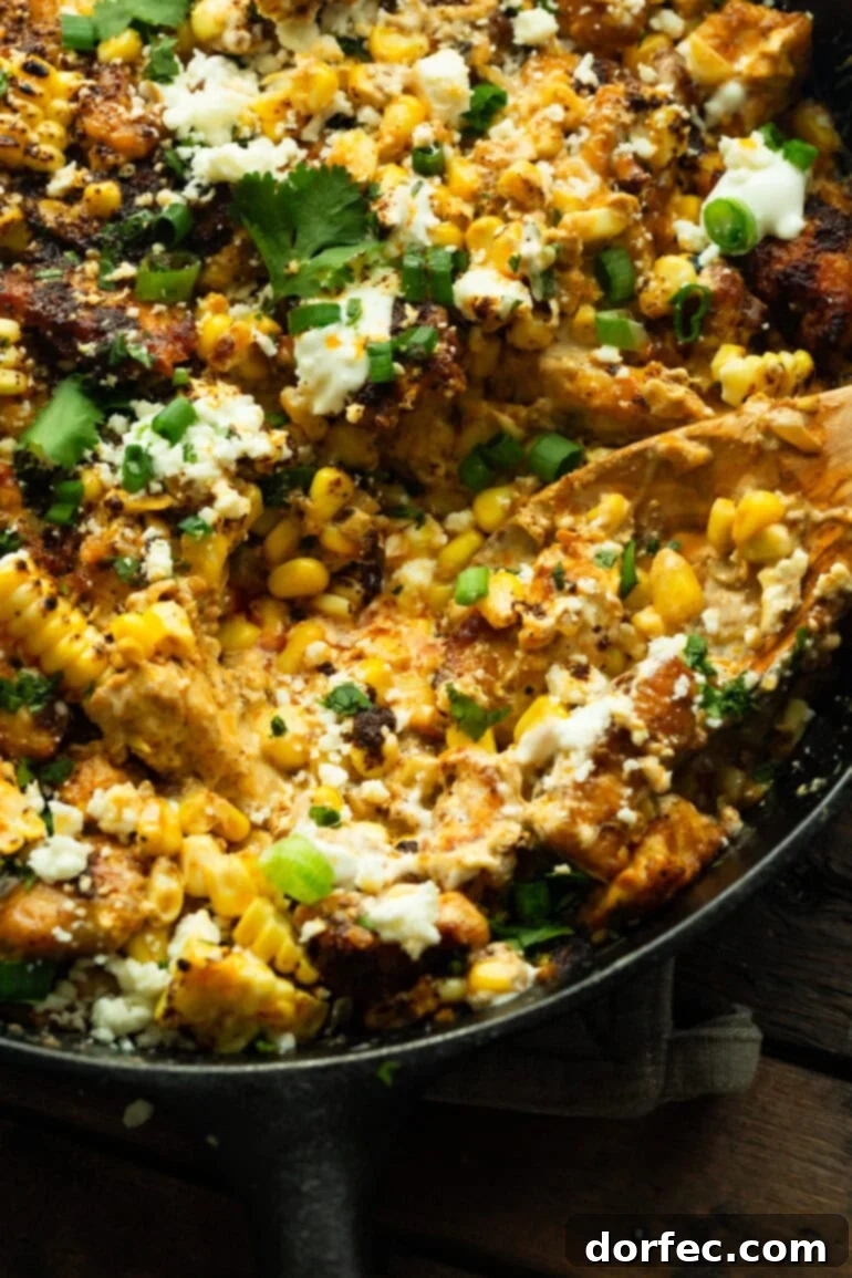 Creamy Mexican Street Corn Chicken Skillet 3 A wooden spoon lifting a serving of creamy Mexican street corn chicken from a cast iron skillet, showcasing the rich texture and vibrant colors.