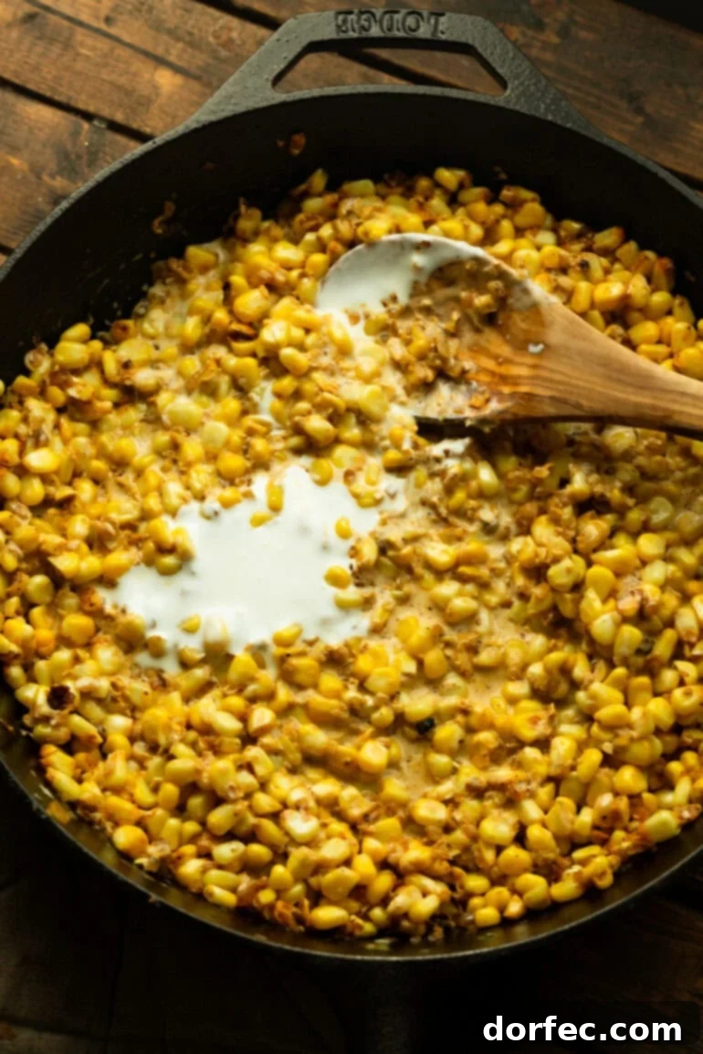Creamy Mexican Street Corn Chicken Skillet 7 Creamy Mexican crema being stirred into sautéed corn and spices in a cast iron skillet.