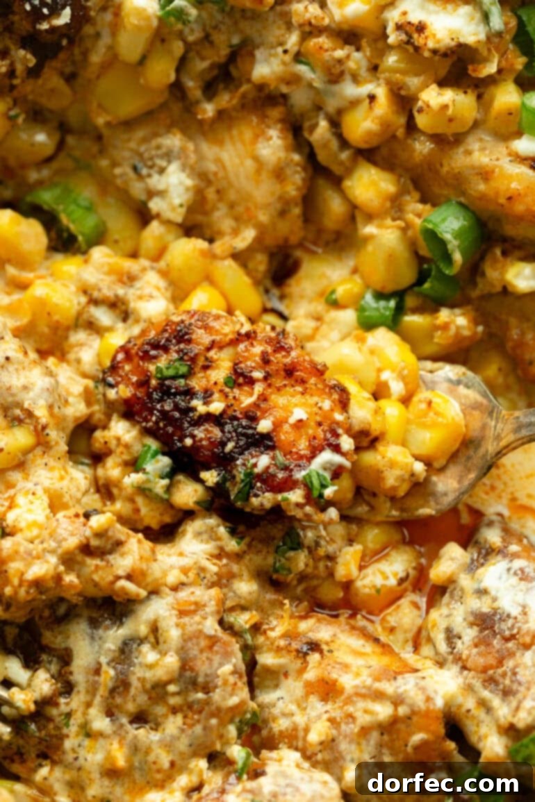 Creamy Mexican Street Corn Chicken Skillet 8 A scoop of creamy Mexican street corn chicken being lifted from a full cast iron skillet, ready to be served.