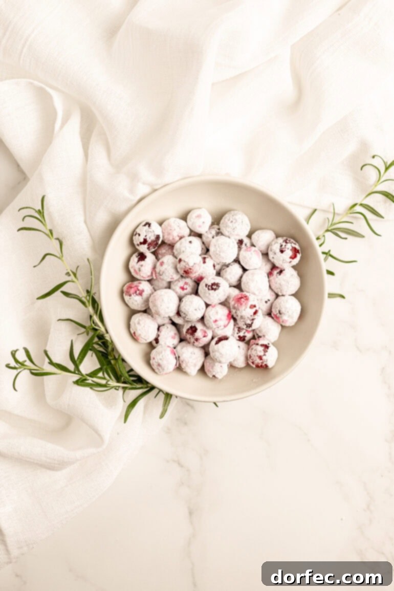 Glittering Sweet Tart Cranberries 9 A charming small bowl brimming with glistening candied cranberries, artfully arranged with sprigs of fresh rosemary underneath, all set on a pristine white tablecloth, exuding a festive holiday ambiance.