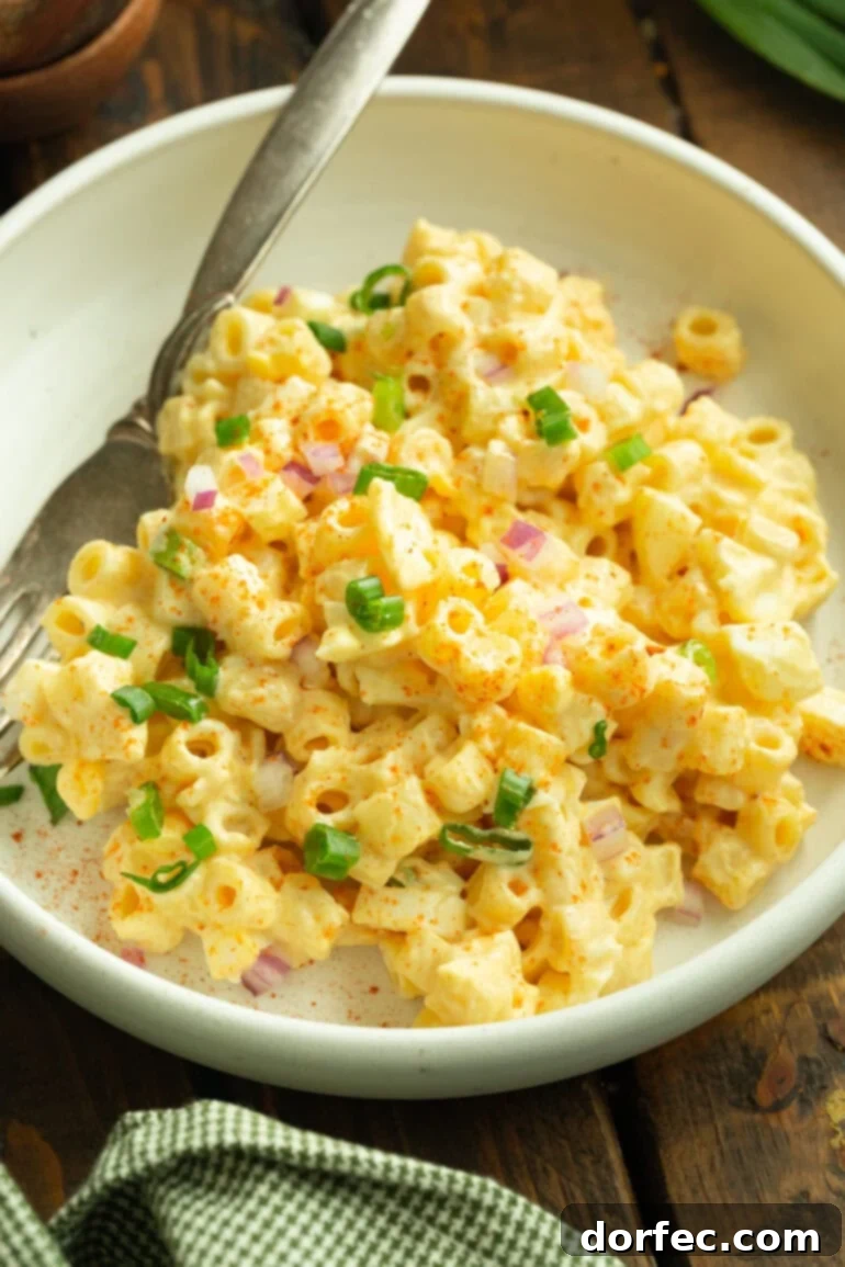 A close-up photo of a single serving of deviled egg pasta salad, presented in a shallow white bowl with a fork resting beside it, garnished with fresh herbs.