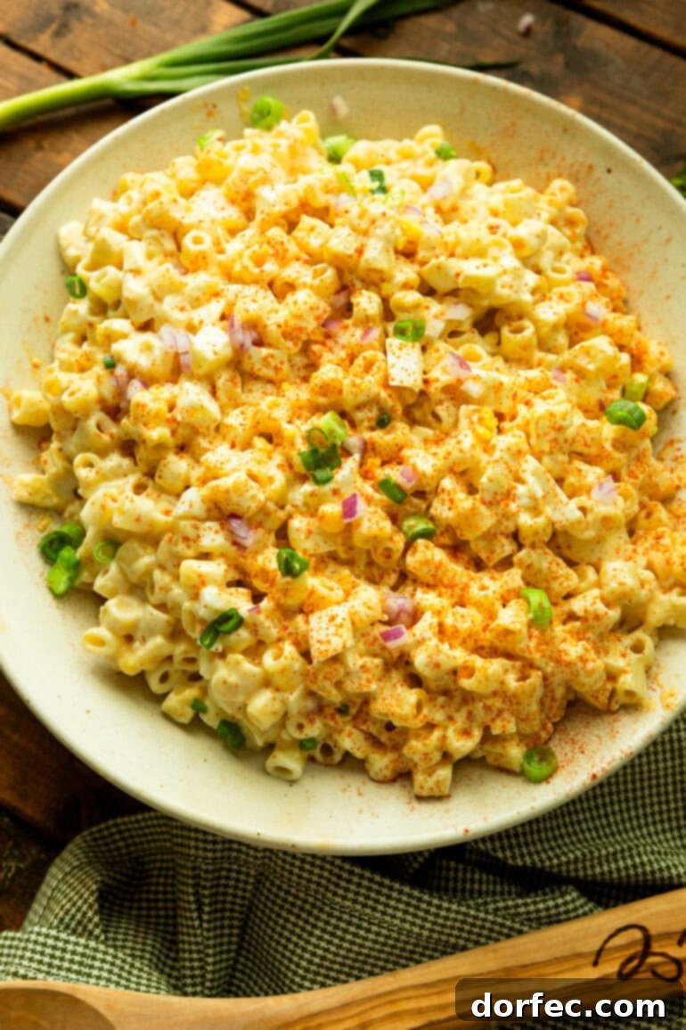 A close-up of deviled egg pasta salad generously topped with chopped green onions and finely diced red onions, showcasing its vibrant freshness.