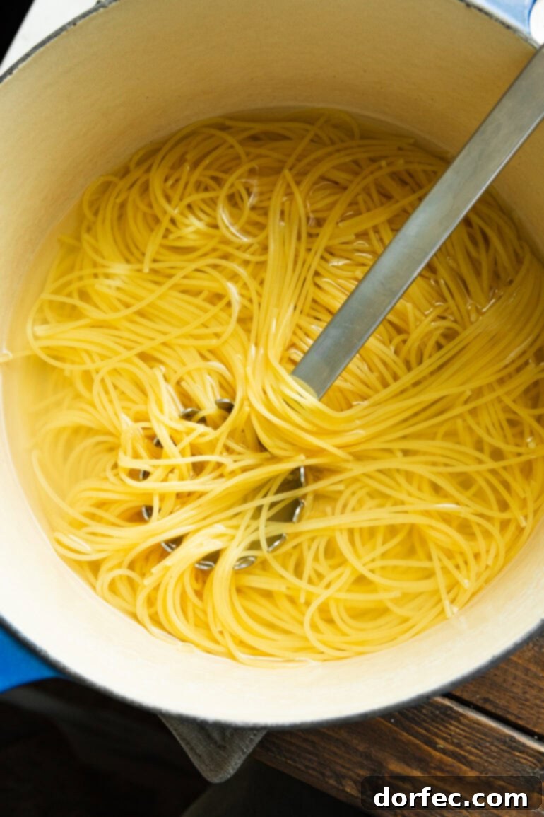 A large pot of perfectly cooked spaghetti noodles being stirred with a metal spoon, showcasing the ideal al dente texture before being combined with the savory Korean ground beef sauce.