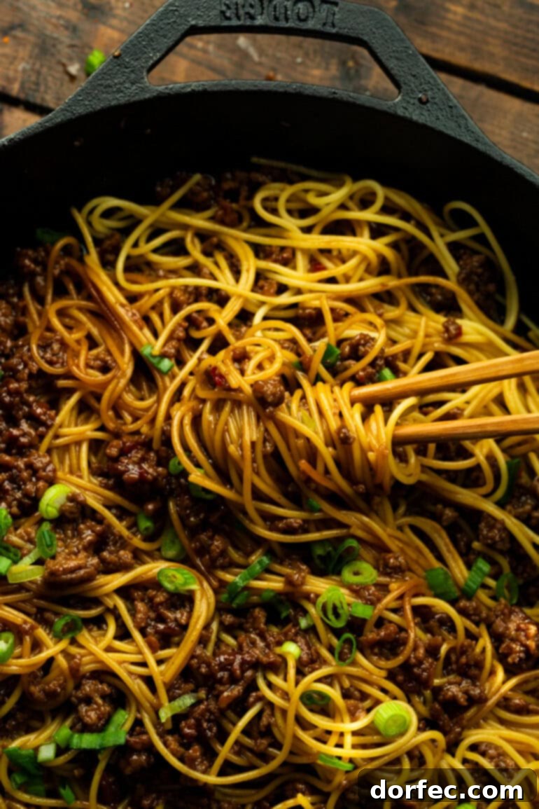 A pair of chopsticks delicately tossing saucy Korean ground beef noodles in a bowl, highlighting the dish's irresistible texture and readiness to eat.