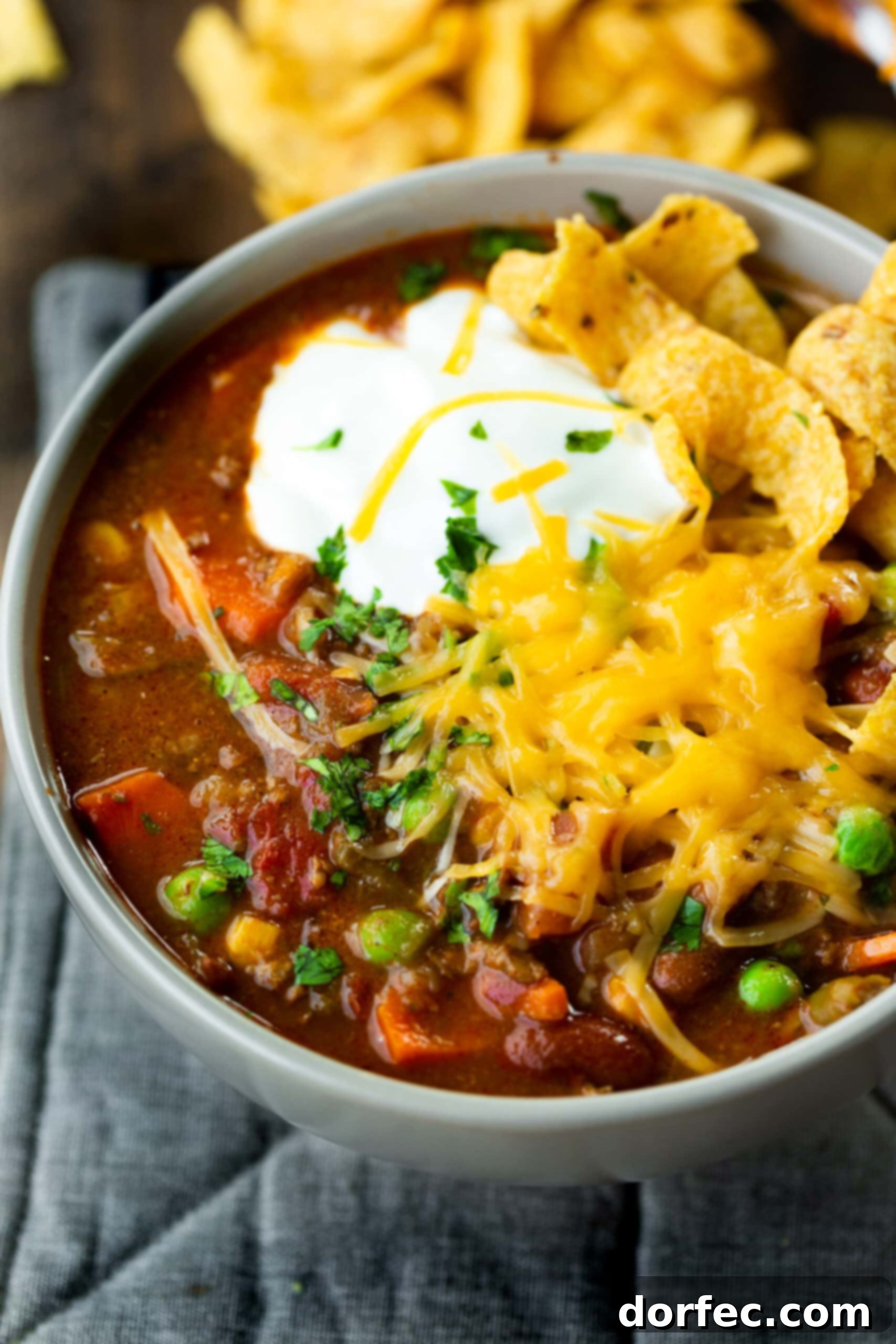 Delicious Taco Stew with Toppings A vibrant bowl of hearty taco stew, generously topped with a dollop of cool sour cream, a mound of shredded cheddar cheese, and crispy Fritos chips, ready to be enjoyed.