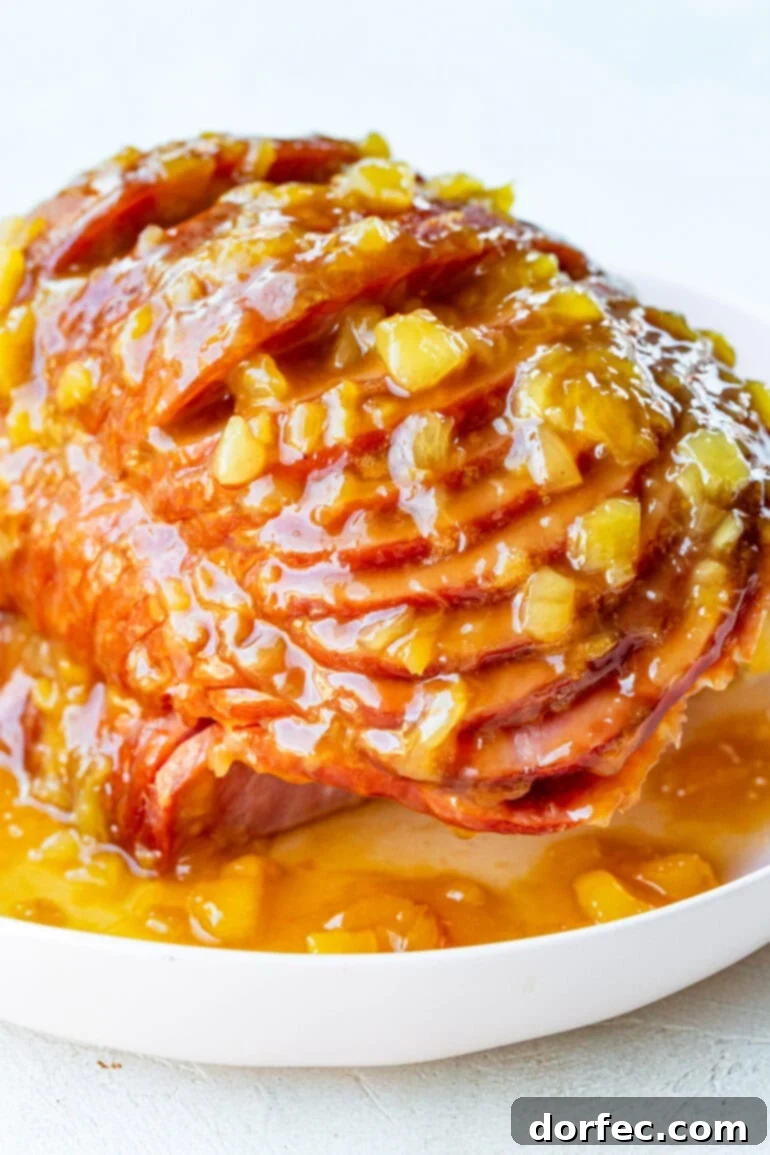 Perfectly Tender Slow Cooker Ham 2 A photo of a spiral cut ham topped with a juicy pineapple glaze on a large white serving platter, ready to be served for a festive occasion.