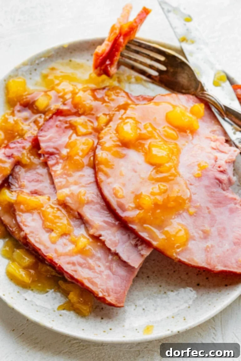 Perfectly Tender Slow Cooker Ham 3 A close-up photo of several slices of perfectly cooked slow cooker ham, generously topped with a rich, shimmering pineapple glaze, showcasing its tender texture.