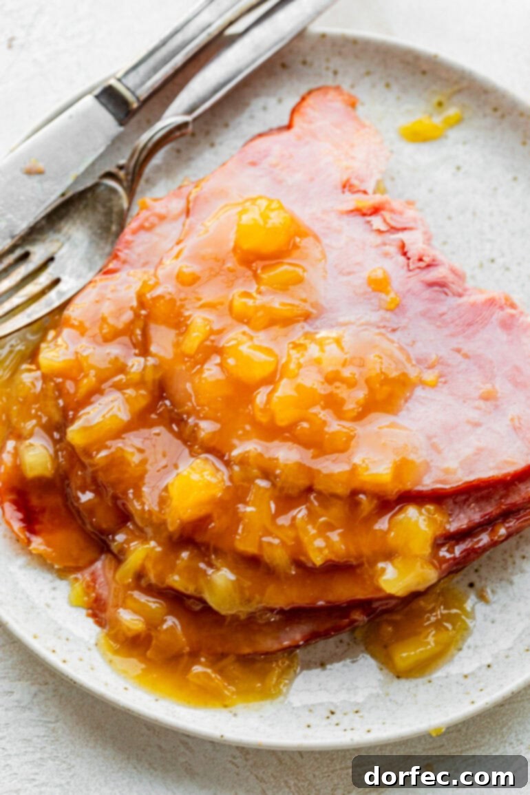 Perfectly Tender Slow Cooker Ham 6 A beautifully composed photo featuring several slices of tender ham arranged on a white plate, elegantly topped with a glistening pineapple glaze. A fork rests beside the plate, ready for dining.