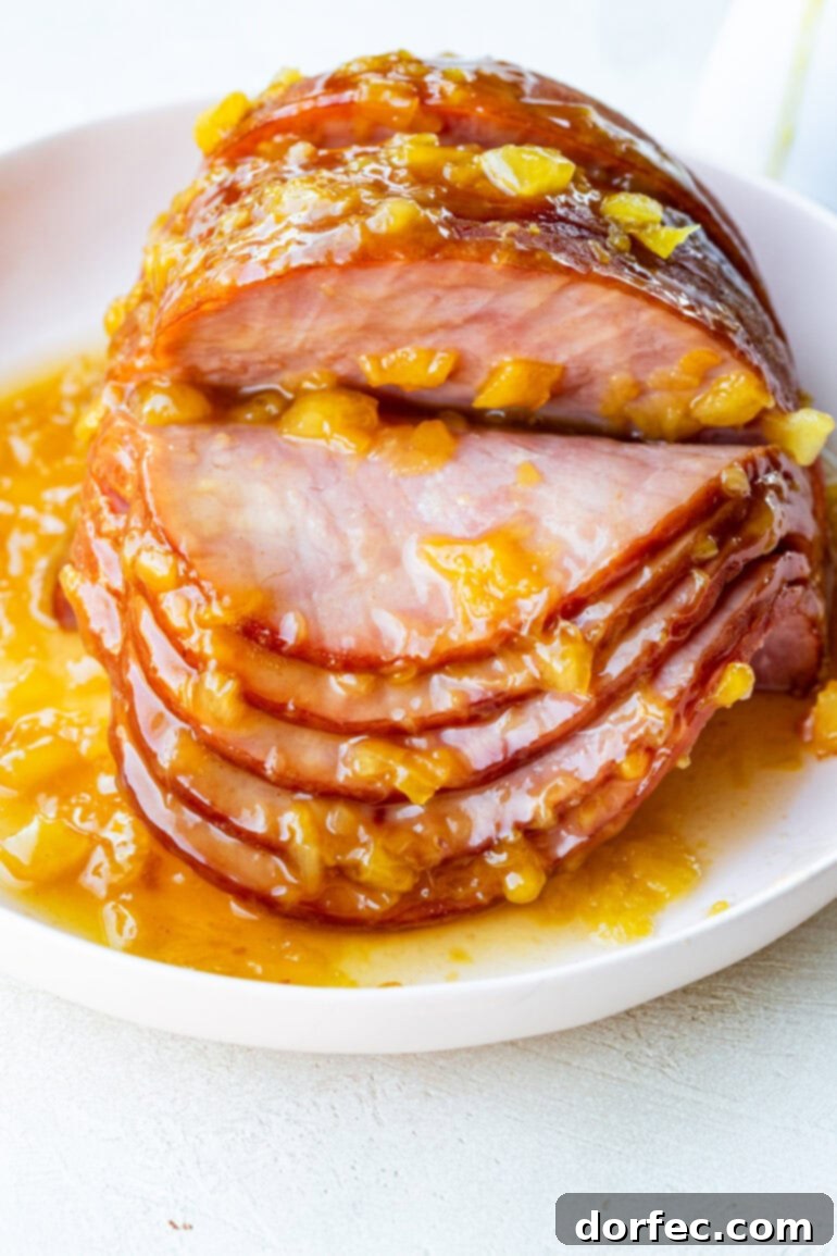 Perfectly Tender Slow Cooker Ham 9 A stunning photo of a whole spiral ham, beautifully arranged on a white serving plate, generously topped with a glistening pineapple glaze, with several perfectly carved slices fanned out beside it.