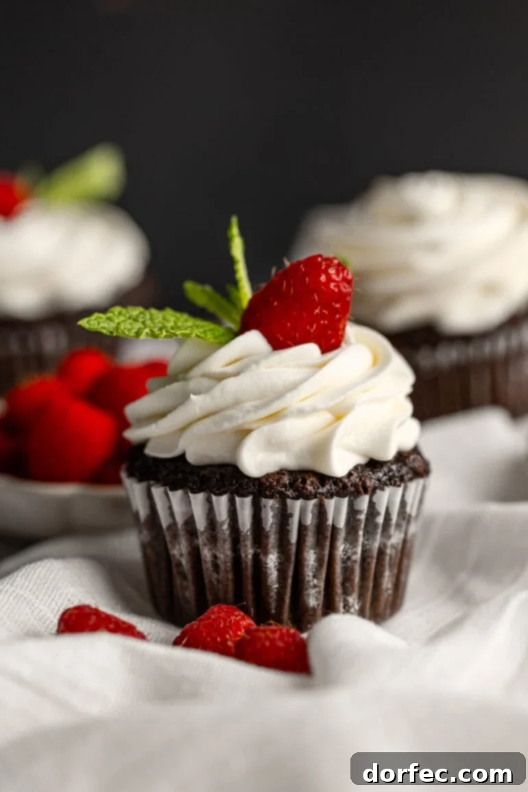 Fluffy Tangy Cream Cheese Frosting 11 A delectable chocolate cupcake, nestled in its liner, exquisitely topped with a generous swirl of piped cream cheese frosting, garnished with a single vibrant raspberry and a few fresh mint leaves.