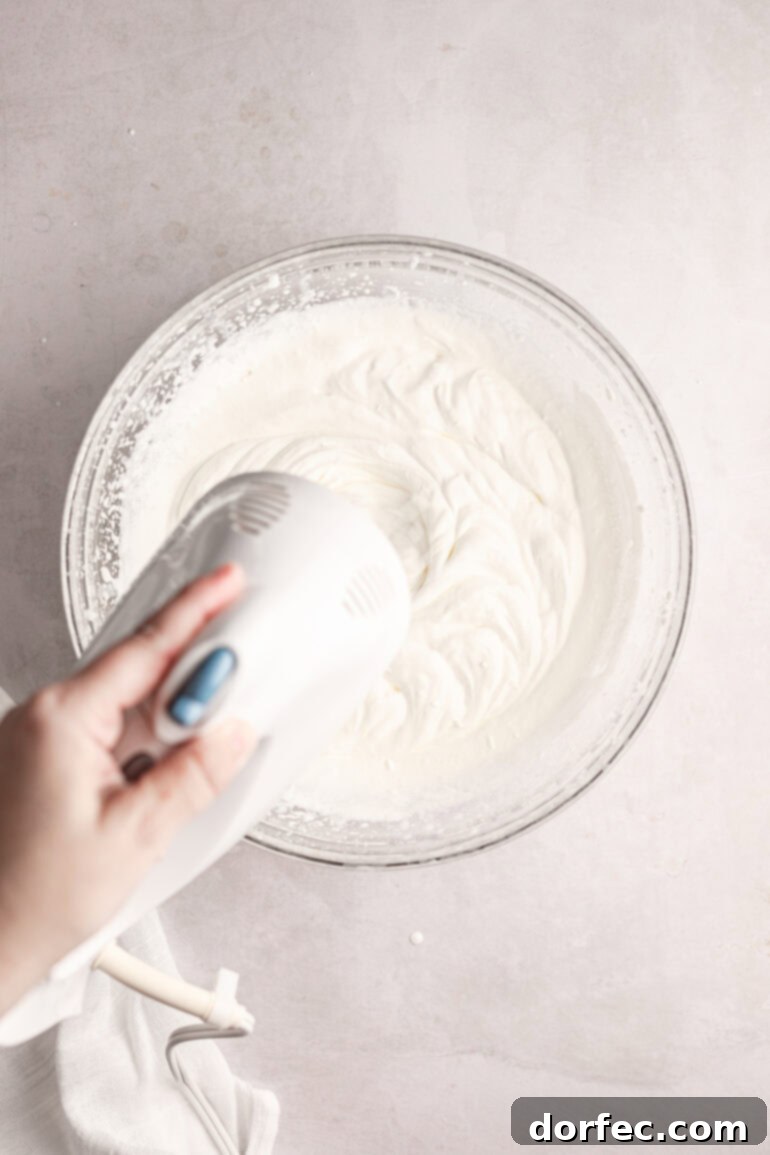 Fluffy Tangy Cream Cheese Frosting 4 Step 1: Beating cold heavy cream in a stand mixer bowl until it forms stiff peaks, demonstrating the initial phase of frosting preparation.