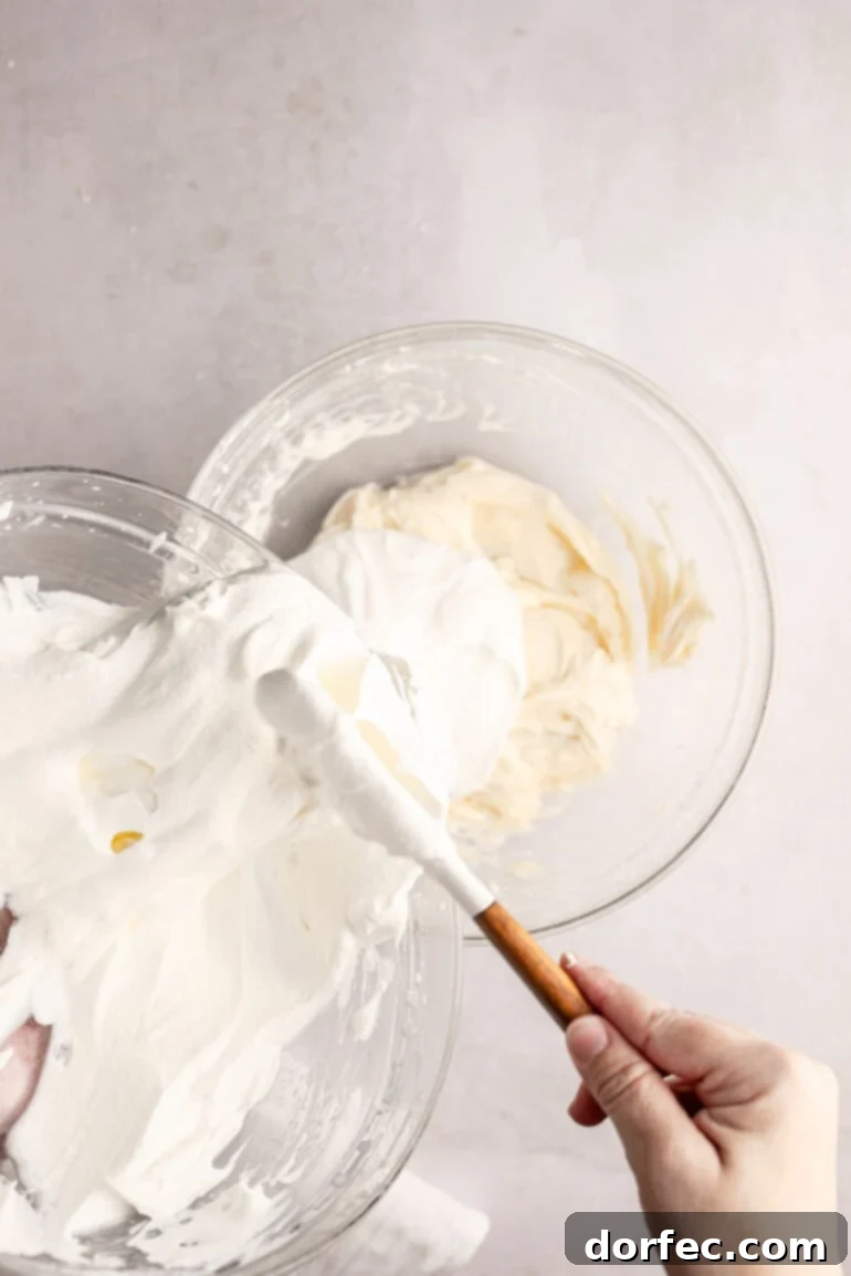 Fluffy Tangy Cream Cheese Frosting 7 Step 4: The stiffly whipped cream being gently added to the creamy cream cheese base, setting the stage for folding.