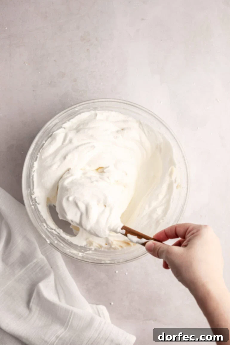 Fluffy Tangy Cream Cheese Frosting 8 Step 5: A spatula performing the crucial folding technique, carefully incorporating the whipped cream without deflating the mixture.