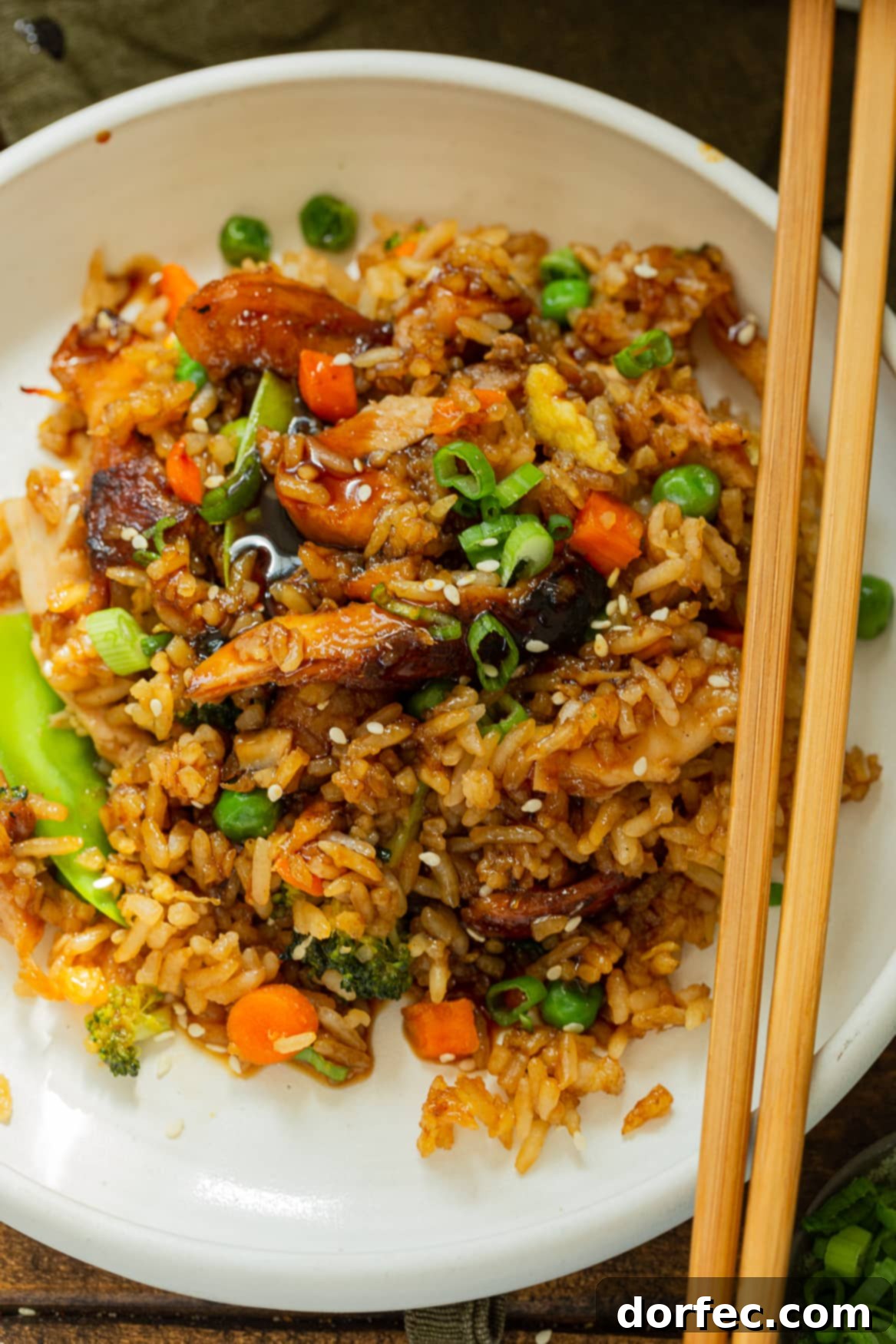 Baked Teriyaki Chicken Casserole: A delicious and easy weeknight dinner idea. A dinner plate brimming with Teriyaki Chicken Casserole, featuring a delectable mix of fried rice, generous chunks of juicy chicken, and an assortment of colorful stir-fried vegetables. Chopsticks rest elegantly on the side of the plate, inviting you to dive into this comforting meal.