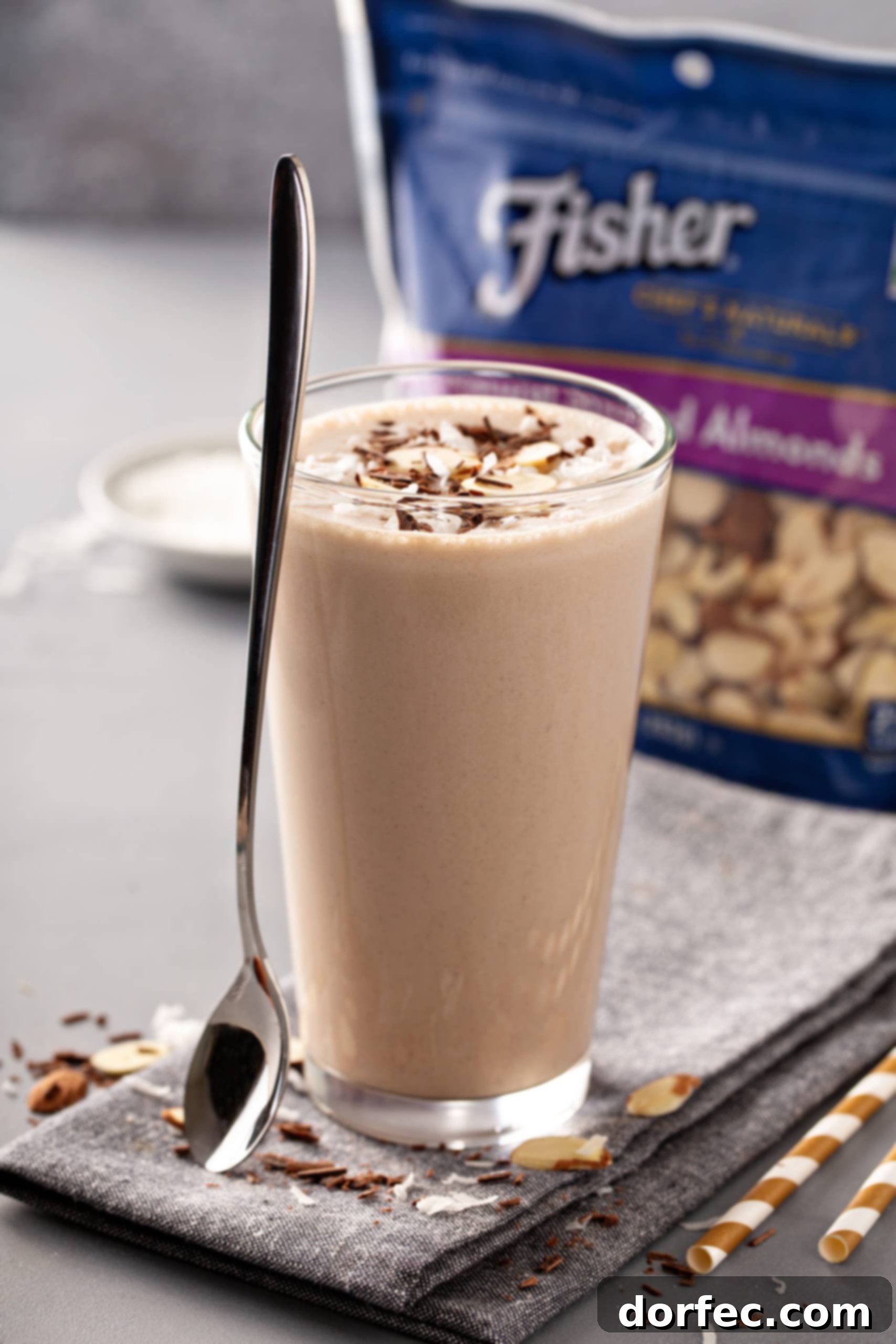 Almond Joy Protein Boost 7 Tall glass of Almond Joy Chocolate Protein Shake with a generous topping of sliced almonds, placed next to a package of Fisher's Sliced almonds on a table.