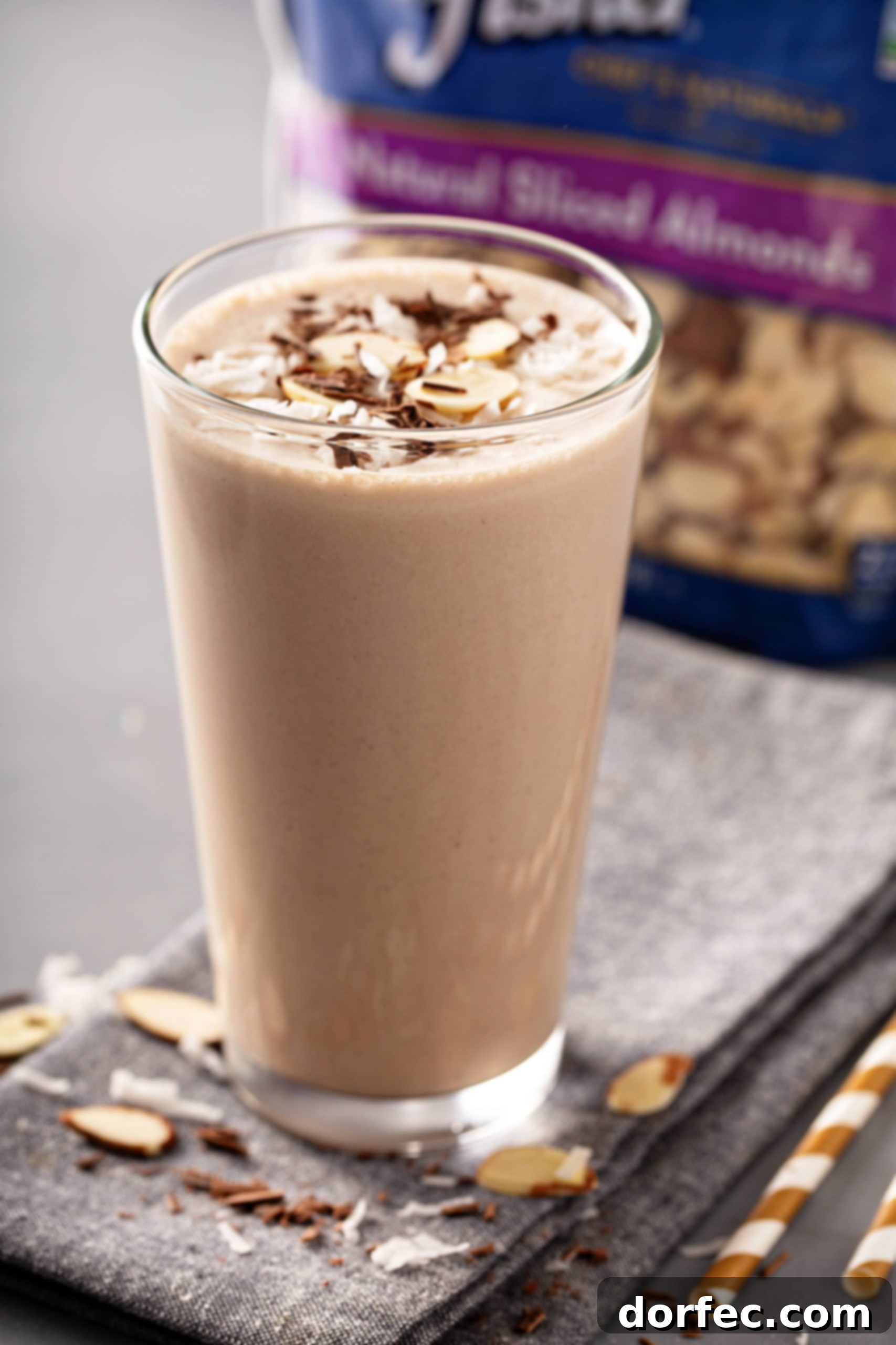 Almond Joy Protein Boost 8 A tall glass of Almond Joy Protein shake with a delightful topping of sliced almonds, set against a blurred background, highlighting its rich and inviting texture.