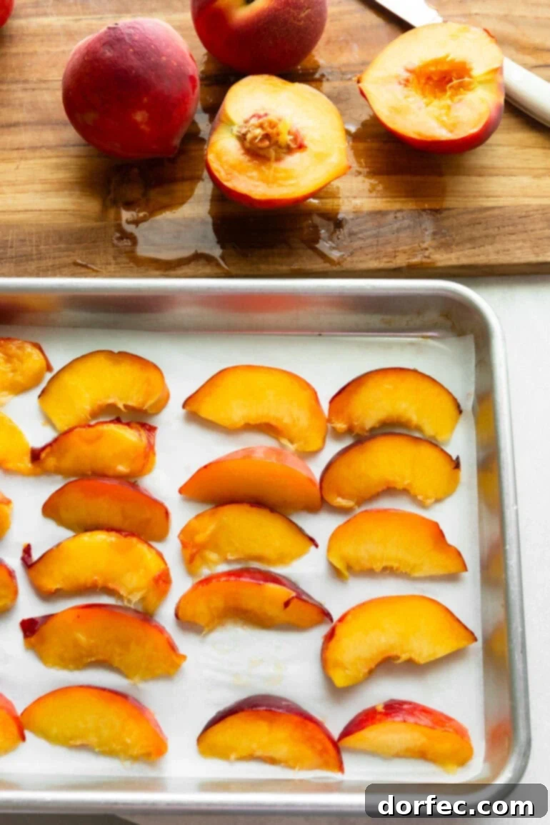 Halved and sliced peaches arranged on a parchment-lined baking sheet before freezing.