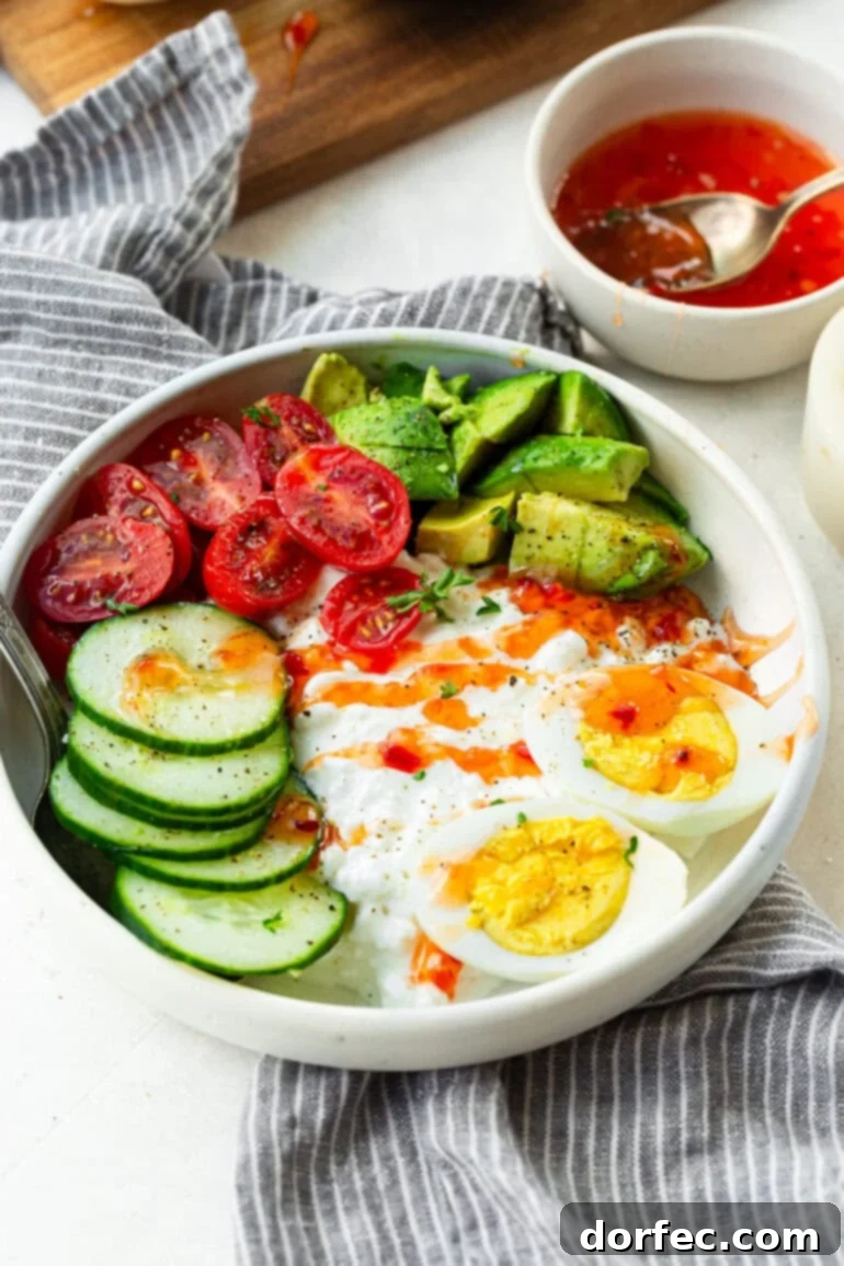 The Trending Protein Power Bowl: Eggs and Cottage Cheese 2 A large bowl filled with creamy cottage cheese, perfectly sliced hard-boiled eggs, fresh cucumber, ripe cherry tomatoes, and a generous topping of avocado, all drizzled with a sweet chili sauce, ready to be enjoyed as a high-protein breakfast.