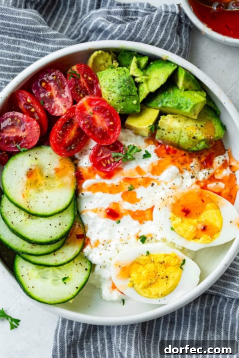 The Trending Protein Power Bowl: Eggs and Cottage Cheese 3 A close-up shot of a savory cottage cheese breakfast bowl, artfully arranged with halved hard-boiled eggs, thin slices of cucumber, juicy avocado chunks, and bright cherry tomatoes, all enhanced with a tantalizing drizzle of sweet chili sauce, showcasing its vibrant freshness and appealing textures.