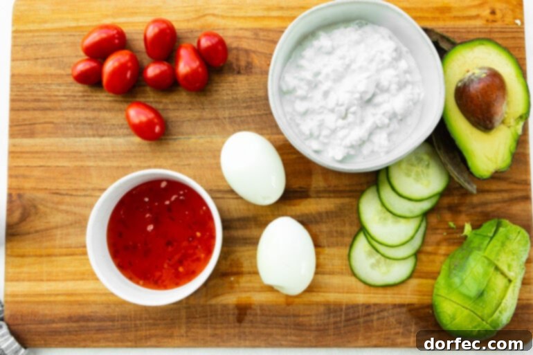 The Trending Protein Power Bowl: Eggs and Cottage Cheese 4 A beautifully arranged flat lay photo showcasing all the fresh and vibrant ingredients required for the high-protein eggs and cottage cheese bowl, including a bowl of creamy cottage cheese, halved hard-boiled eggs, colorful grape tomatoes, crisp cucumber slices, and a bottle of sweet chili sauce, highlighting the simplicity and freshness of the components.