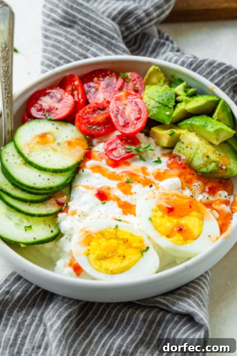 The Trending Protein Power Bowl: Eggs and Cottage Cheese 5 An overhead view of a vibrant high-protein eggs and cottage cheese breakfast bowl, elegantly topped with creamy avocado slices, crisp cucumber, juicy cherry tomatoes, and a savory drizzle of sweet chili sauce, highlighting the fresh ingredients and appealing presentation.