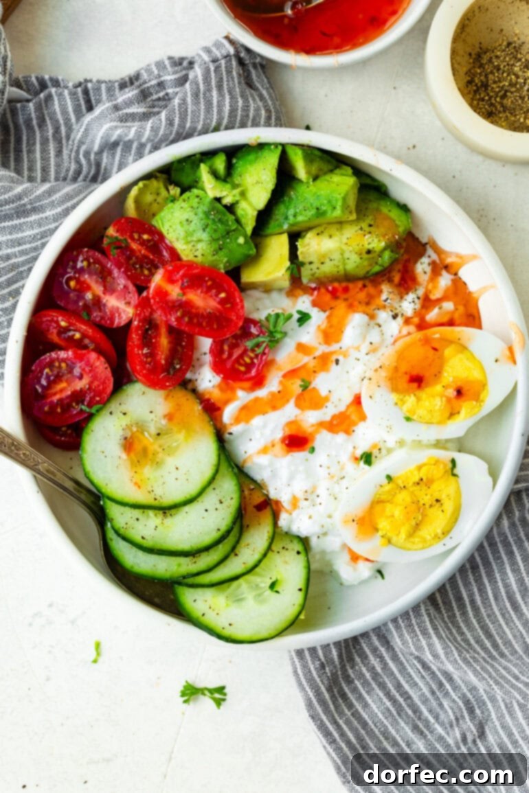 The Trending Protein Power Bowl: Eggs and Cottage Cheese 7 A stunning overhead shot of the completed high-protein eggs and cottage cheese breakfast bowl, garnished with beautiful avocado slices, halved cherry tomatoes, fresh cucumber, and a generous drizzle of sweet chili sauce, presented in a clean and appealing ceramic bowl.