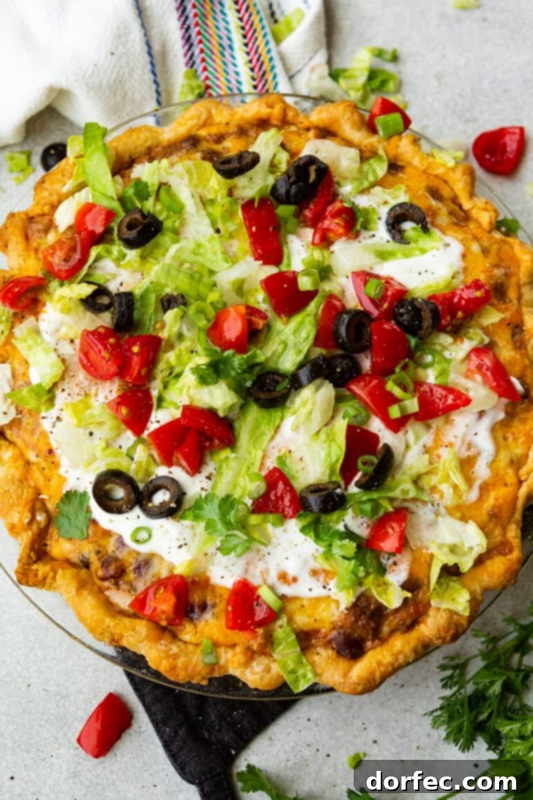 A beautiful whole Taco Pie, showcasing its golden-brown crust, bubbling cheesy ground beef filling, and a colorful array of fresh toppings including sour cream, crisp shredded lettuce, bright diced tomatoes, and dark black olives.