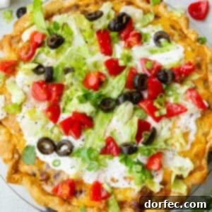 A whole taco pie with a golden crust, cheesy ground beef, topped with sour cream, shredded lettuce, diced tomatoes and black olives