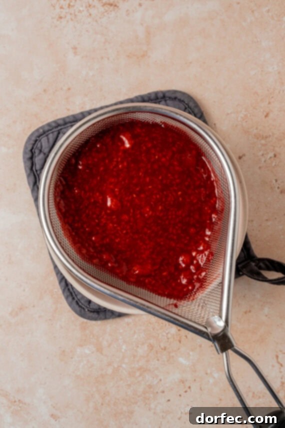 Straining raspberry sauce through a fine mesh sieve to remove seeds.
