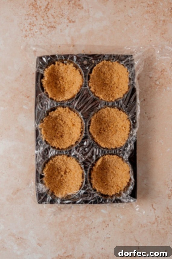 Pressing graham cracker crust into lined muffin tins.