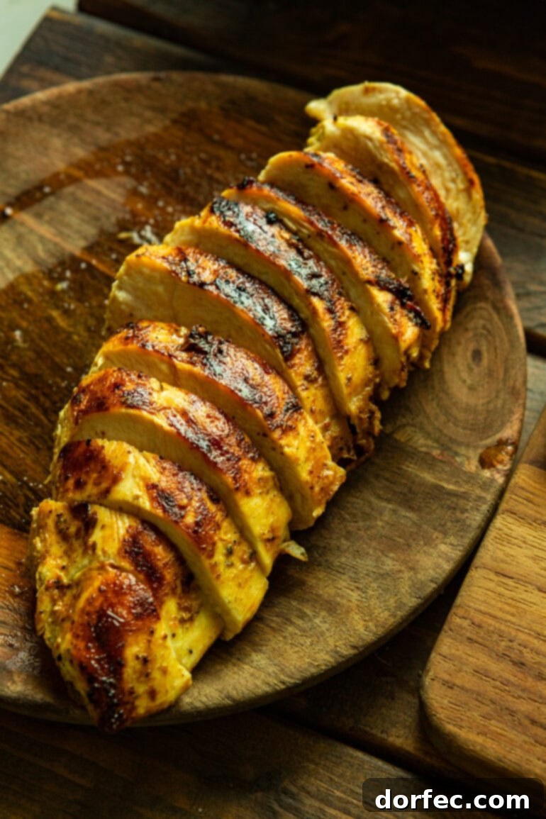 A beautifully sliced grilled chicken breast, displaying its juicy interior and charred edges, resting on a rustic wooden plate, ready to be added to a fresh summer salad.