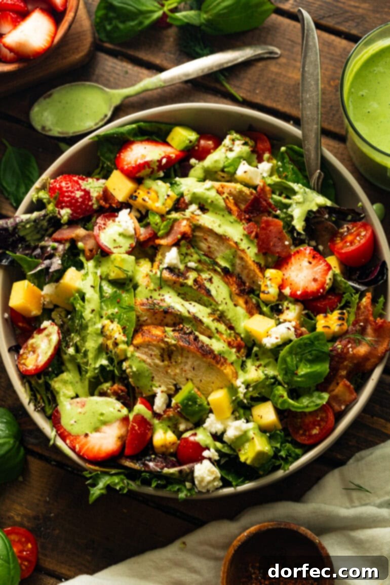 A vibrant and artfully arranged grilled chicken salad, featuring tender chicken, fresh strawberries, crispy bacon, sweet grilled corn, and a mix of cheeses, all generously topped with a luscious basil dressing.