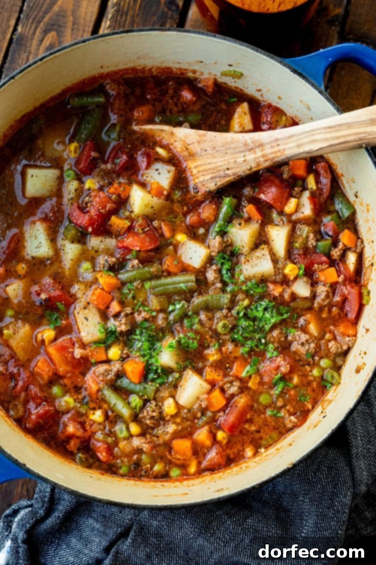 Simple & Satisfying Ground Beef Vegetable Soup 2 A large pot of steaming ground beef vegetable soup, generously garnished with fresh minced parsley, with a wooden spoon invitingly placed within the bowl.