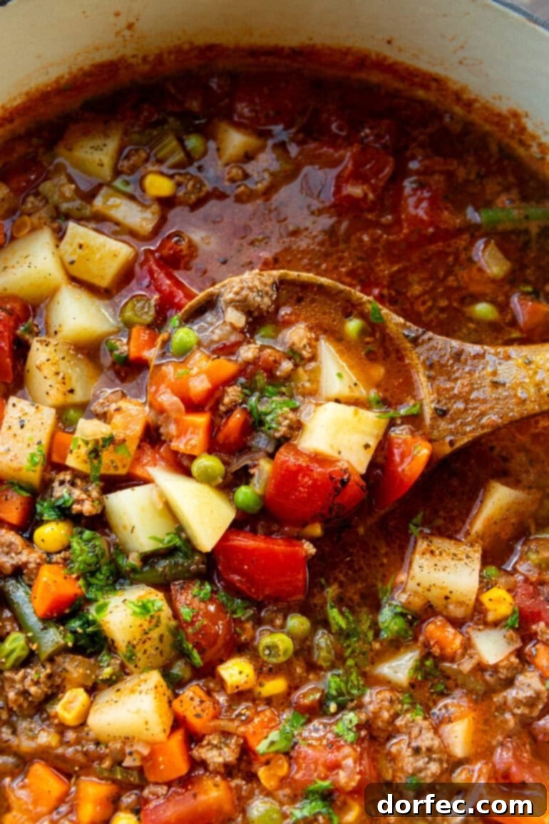 Simple & Satisfying Ground Beef Vegetable Soup 3 A wooden spoon lifting a spoonful of rich ground beef and assorted vegetables from a large pot of hamburger soup, showcasing the hearty texture.
