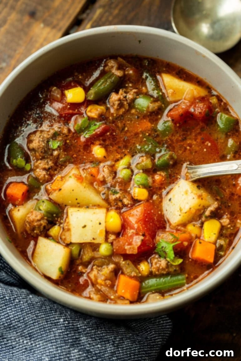 Simple & Satisfying Ground Beef Vegetable Soup 5 A beautifully presented bowl of ground beef vegetable soup, with a spoon nestled within, inviting diners to enjoy its hearty goodness.