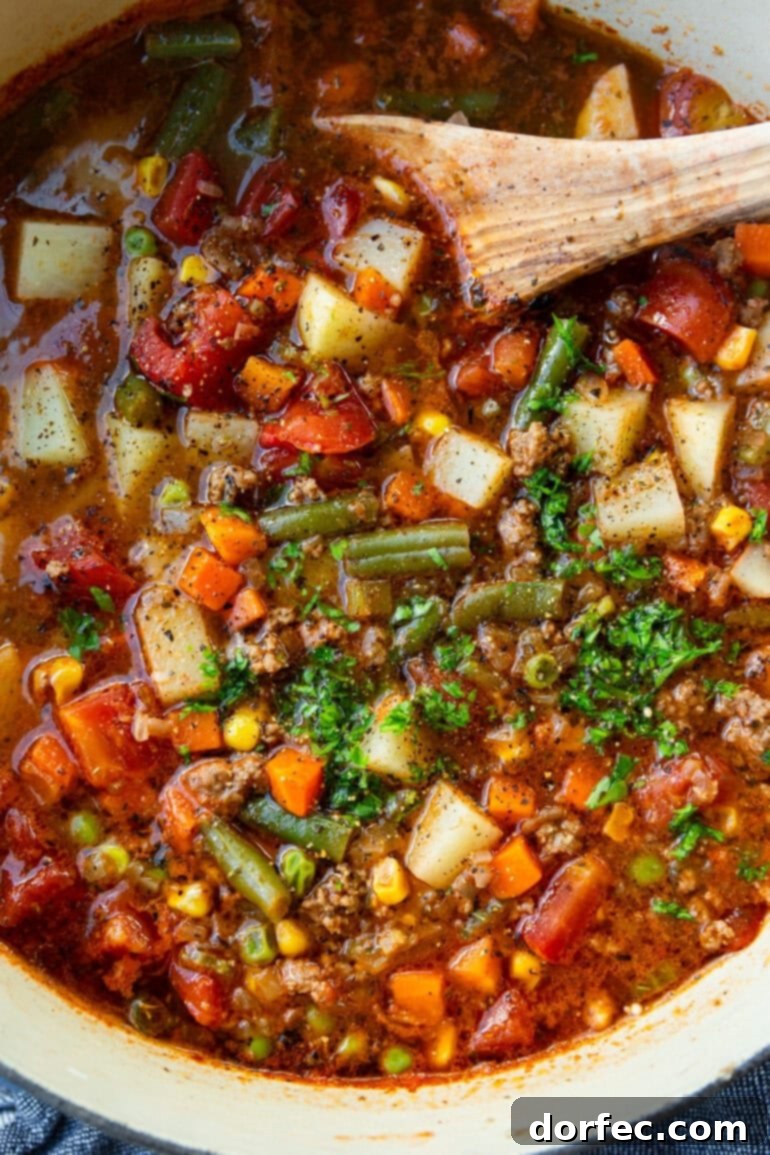 Simple & Satisfying Ground Beef Vegetable Soup 6 A wooden spoon stirring a pot of rich, simmering ground beef vegetable soup, showcasing the vibrant colors of the ingredients.