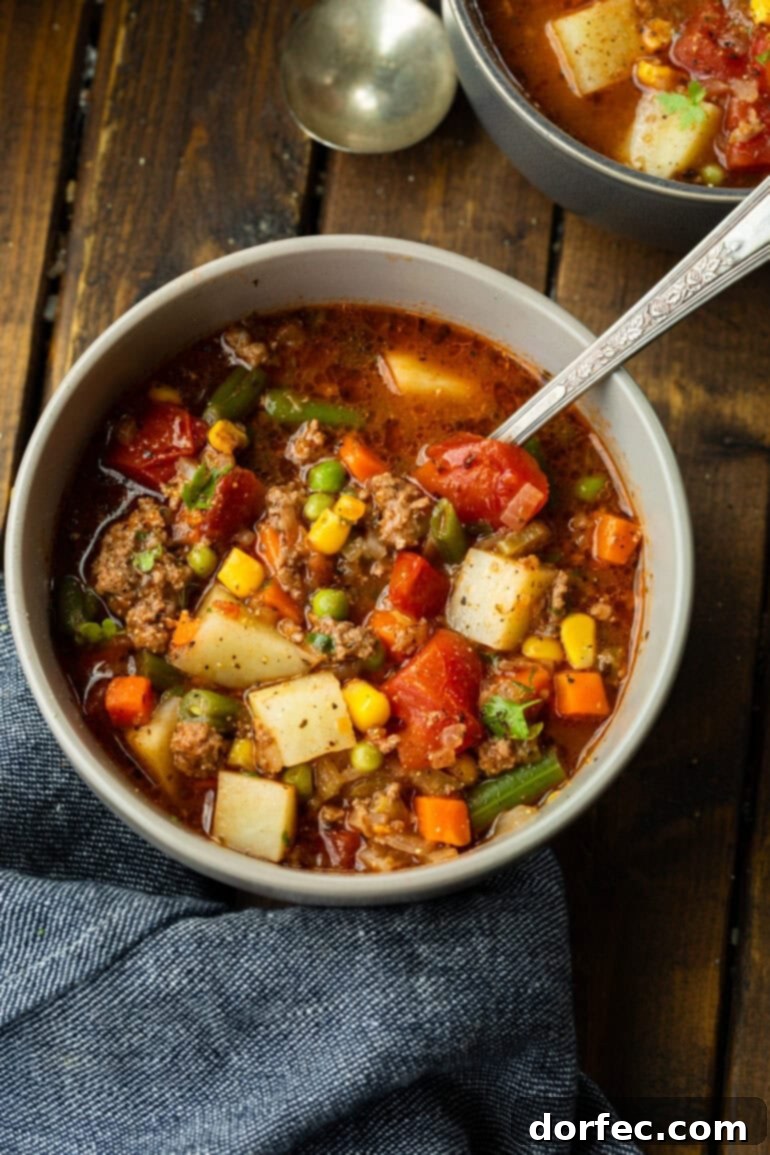 Simple & Satisfying Ground Beef Vegetable Soup 8 A generous bowl filled with rich and hearty ground beef vegetable soup, with a spoon perfectly placed for immediate enjoyment.
