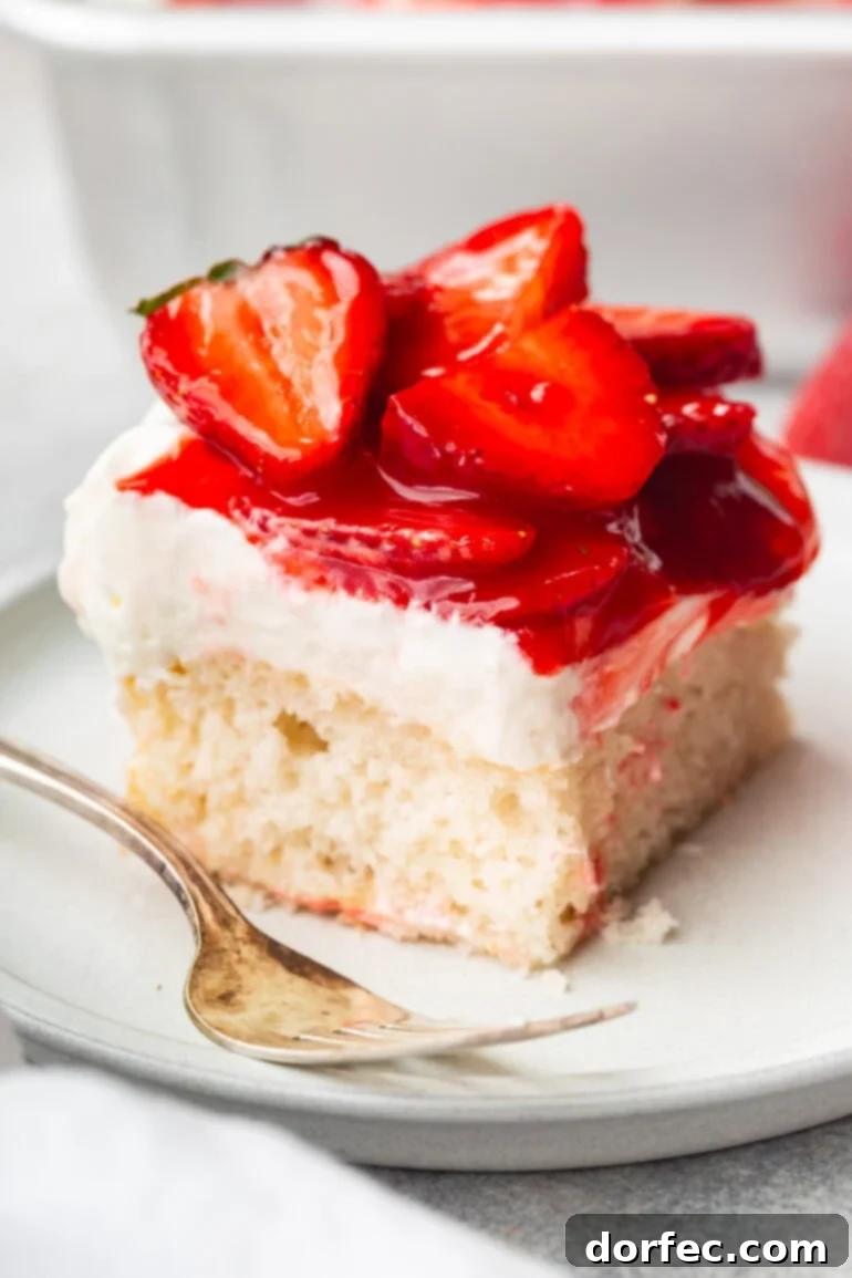 A vibrant slice of moist white cake on a small dessert plate, generously topped with a cloud of cream cheese whipped cream frosting and glistening, juicy red strawberries.