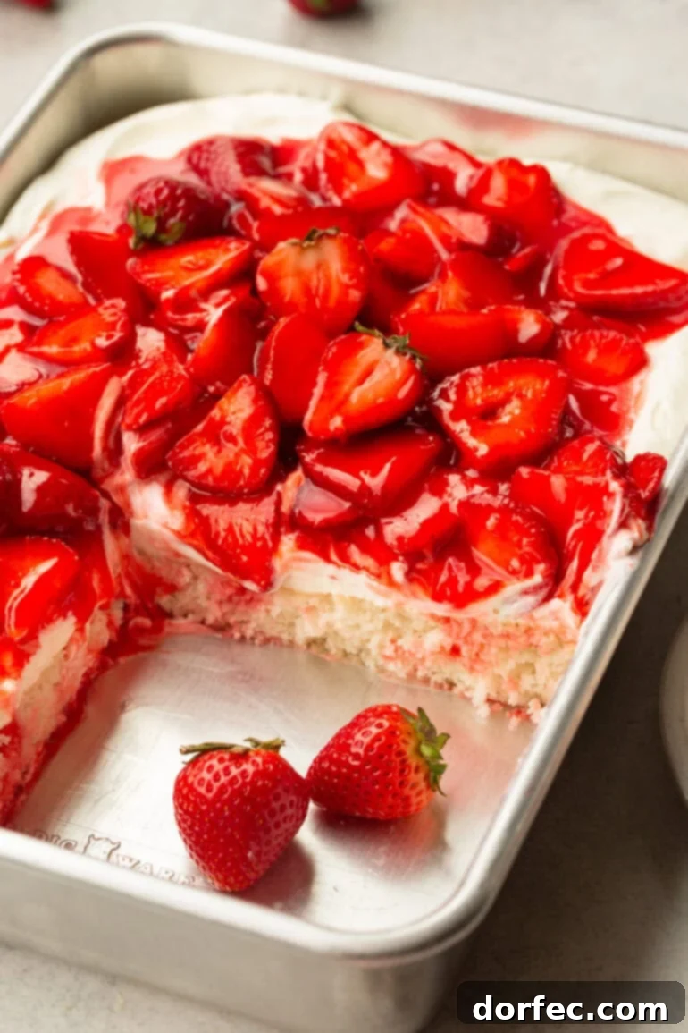 A stunning whole strawberry shortcake cake in a 9x13 inch pan, with one corner slice artfully removed to reveal the exquisite layers of moist white cake, creamy frosting, and vibrant, juicy strawberries.