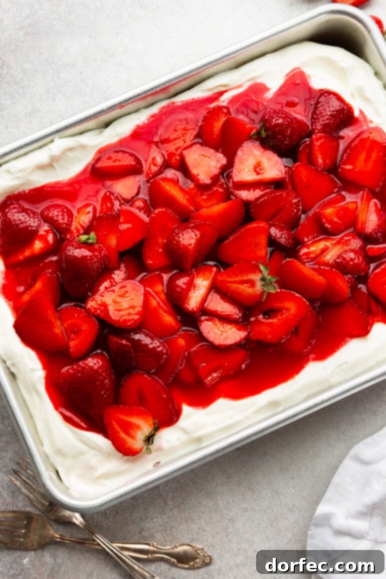 A top-down view of a whole 9x13 strawberry shortcake cake, lavishly covered with creamy frosting and an abundance of glistening, juicy, and saucy strawberries, ready to be served.