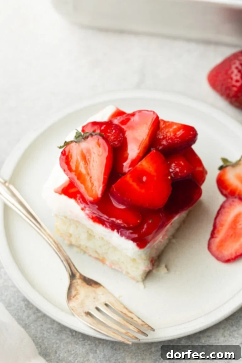 An inviting overhead photo of a single piece of moist white cake, lavishly topped with creamy cream cheese frosting and perfectly sauced, sliced strawberries, showcasing its delectable layers.