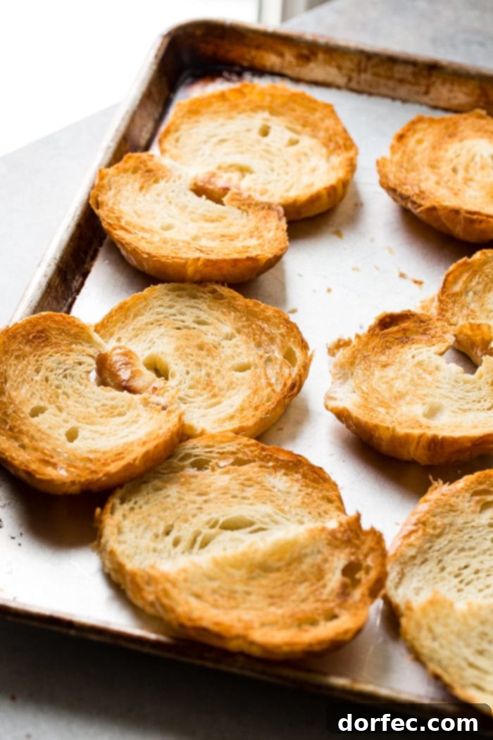 A close-up photo of several croissants sliced horizontally and lightly toasted to a beautiful golden brown, showcasing their flaky texture.