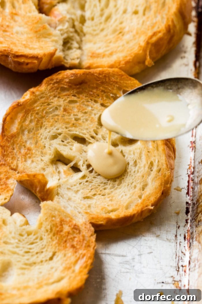 A delectable maple mustard sauce being generously spooned onto a lightly toasted, golden-brown croissant half.