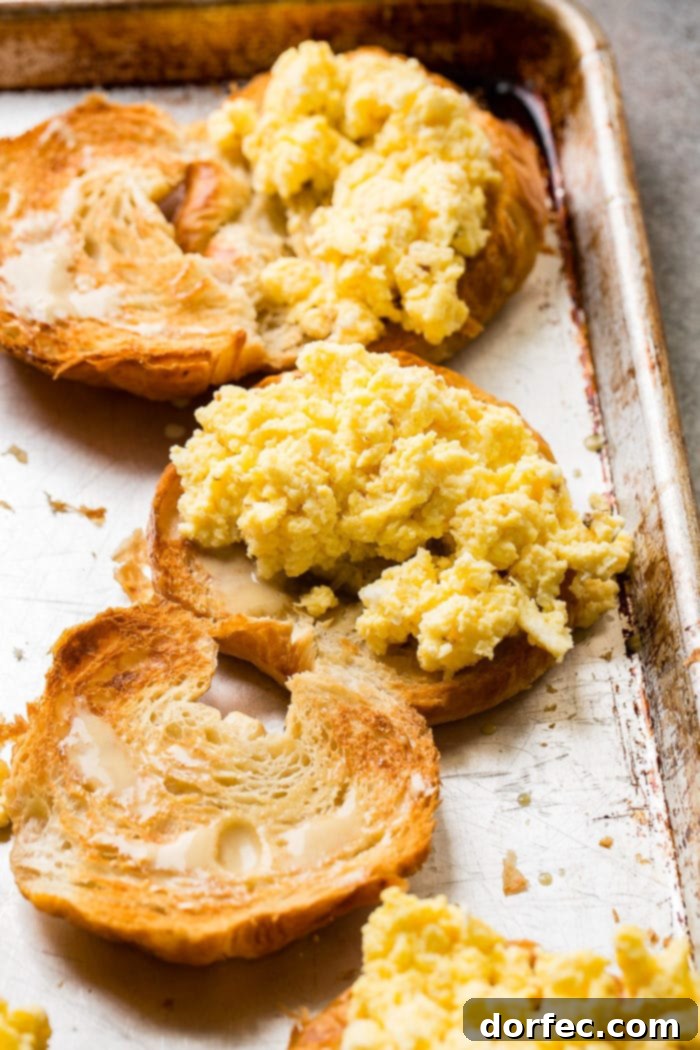 A close-up photo of halved toasted croissants, with one half piled high with perfectly scrambled, fluffy, and golden yellow eggs.