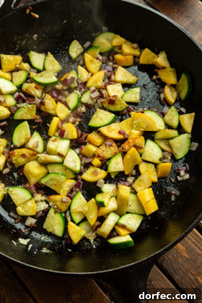Close-up of vibrant zucchini and yellow squash pieces lightly sautéing in a hot cast iron skillet, developing a perfect golden sear.