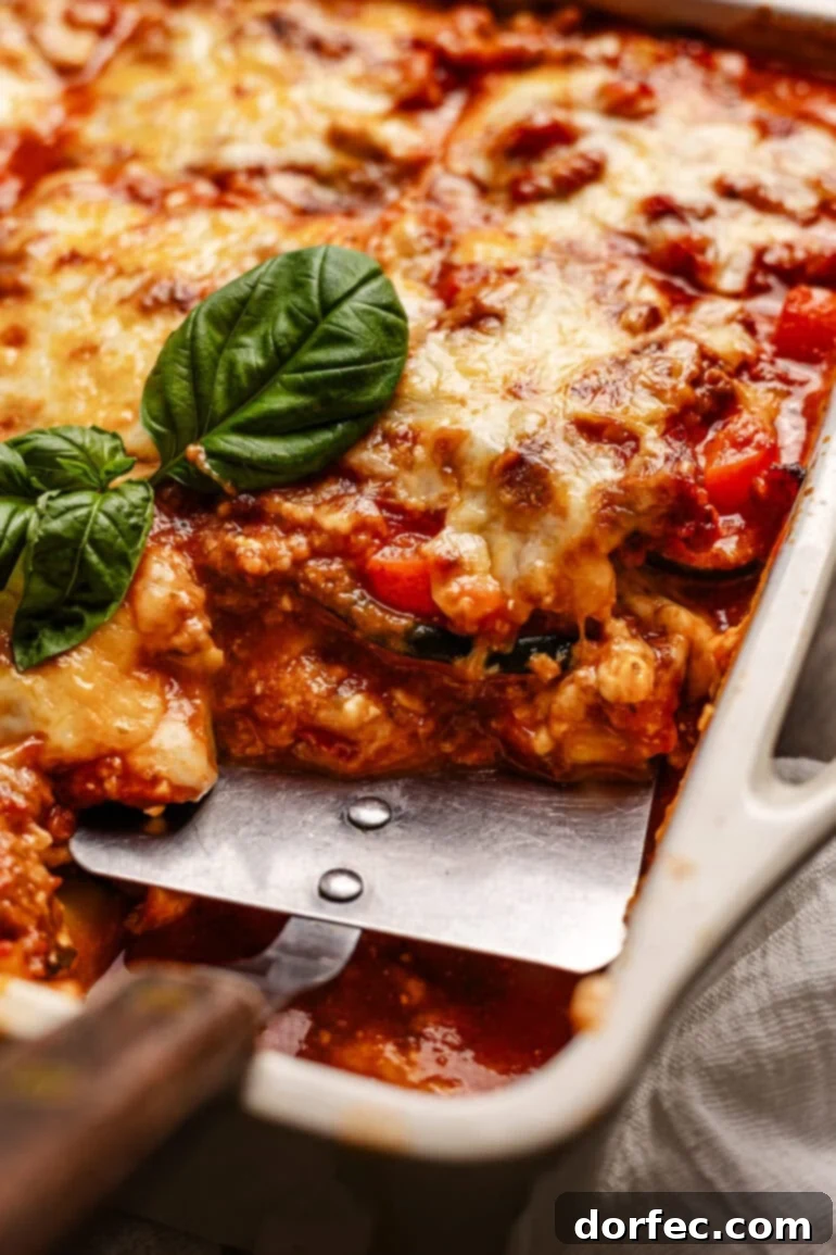 a metal spatula is digging into a full baking dish of layered veggies, meat sauce, and cheese.