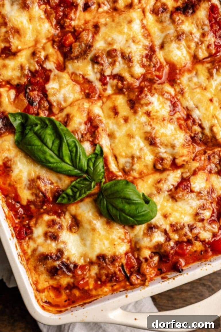 A pan of layered veggie noodles, cheese, and meat sauce that has been baked in the oven with a basil garnish.