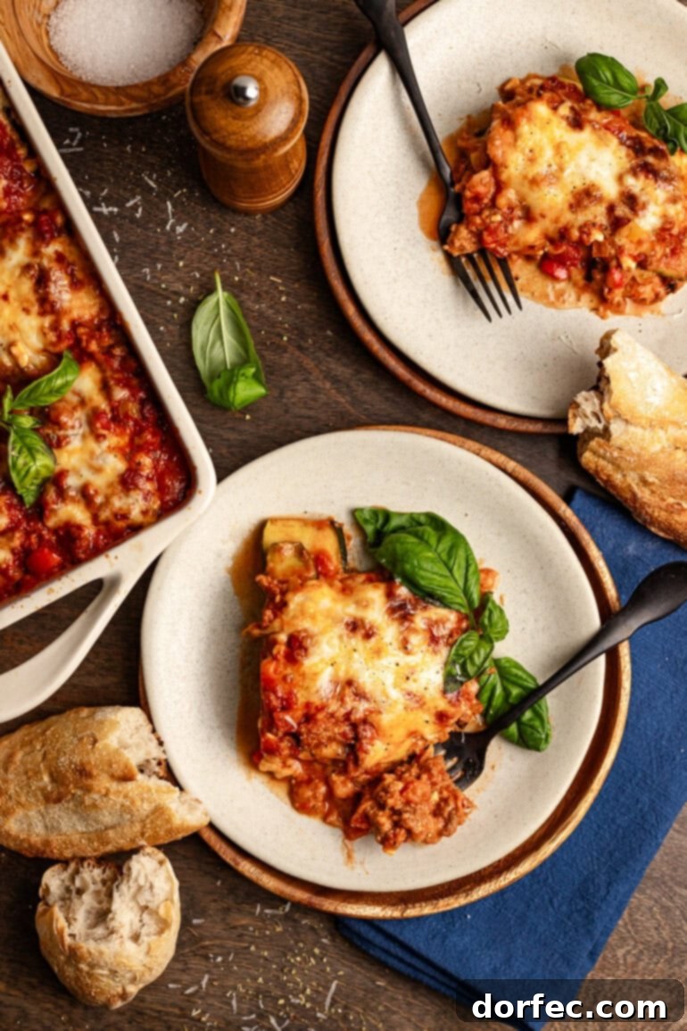 two plates are sitting aside a large baking dish full of zucchini lasagna. each of the plates has a large serving of the dish and a fork.