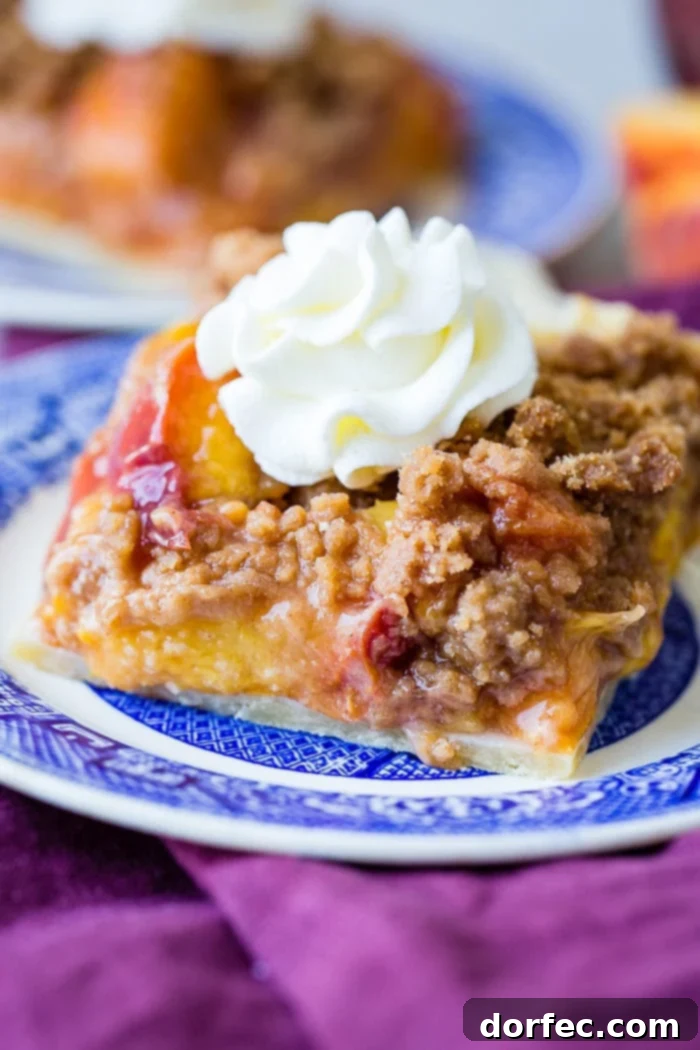 A purple napkin under a vibrant blue china designed dessert plate with a slice of brown sugar peach pie bars with a piped whipped cream dollop on top, evoking a sense of classic summer indulgence.